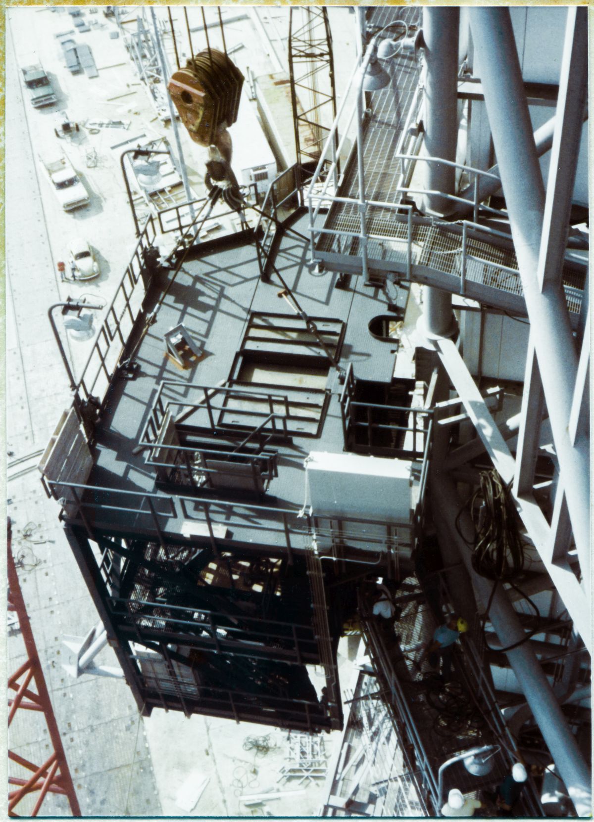 Image 094. Viewed from above, from the Camera Platform at Elevation 260'-0” on the Side 1-2 Corner of the FSS at Space Shuttle Launch Complex 39-B, Kennedy Space Center, Florida, the OMBUU Lift is nearing it final stage, at which point it will be bolted to the RSS by Union Ironworkers working for Ivey Steel. At this point the OMBUU is not quite where it belings, and the Lift has been halted by an unexpected interference condition (not visible in the photograph), and work is ongoing to rectify the situation and complete the task in a timely manner. Photo by James MacLaren.